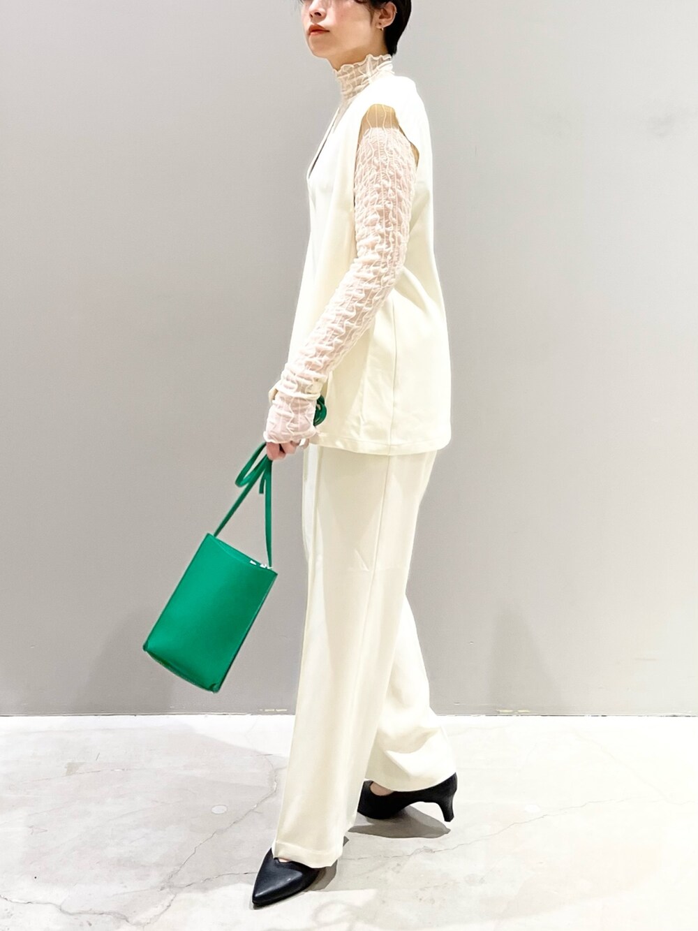 ホワイト系のベスト、グレー系のシューズ、グリーン系のバッグを着用したレディースの夏コーディネートの4枚目の写真