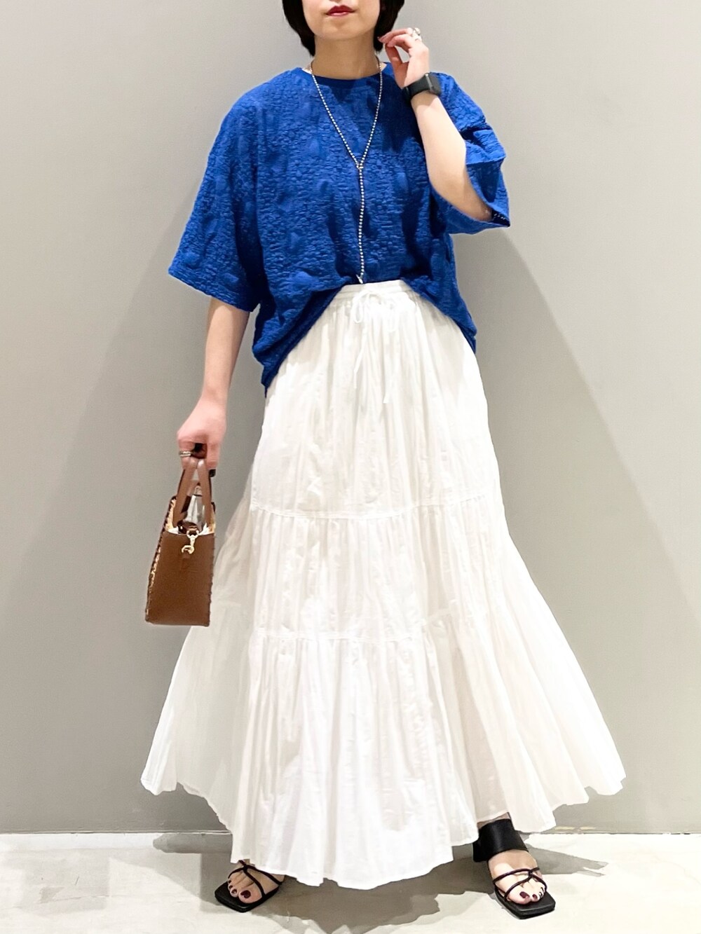 ブラック系のサンダル、ブラウン系のショルダーバッグ、ホワイト系のスカートを着用したレディースの夏コーディネートの7枚目の写真