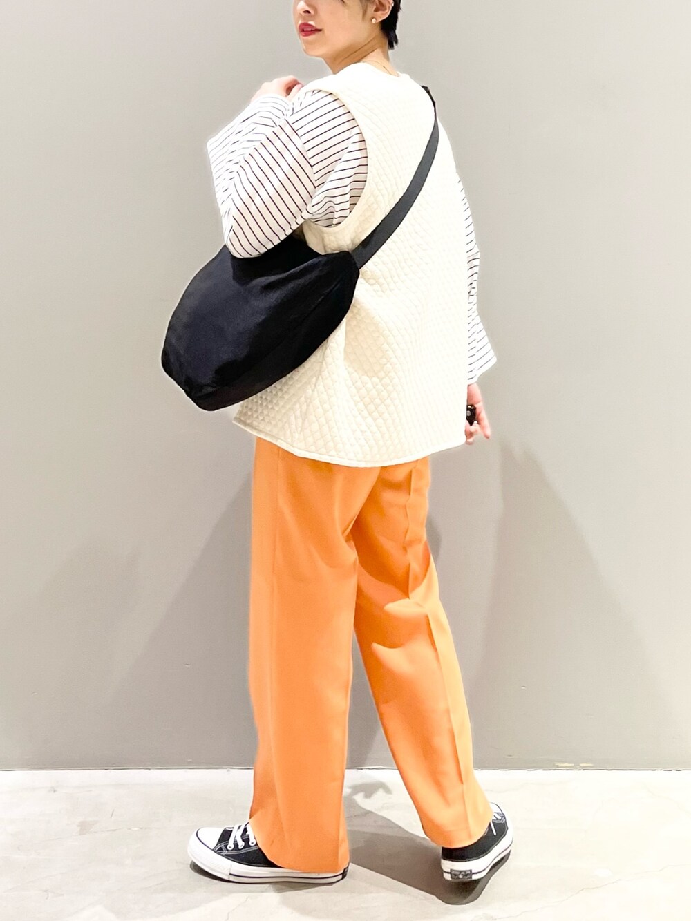 ブラック系のスニーカー、オレンジ系のスラックス、ホワイト系のトップスを着用したレディースの春コーディネートの3枚目の写真