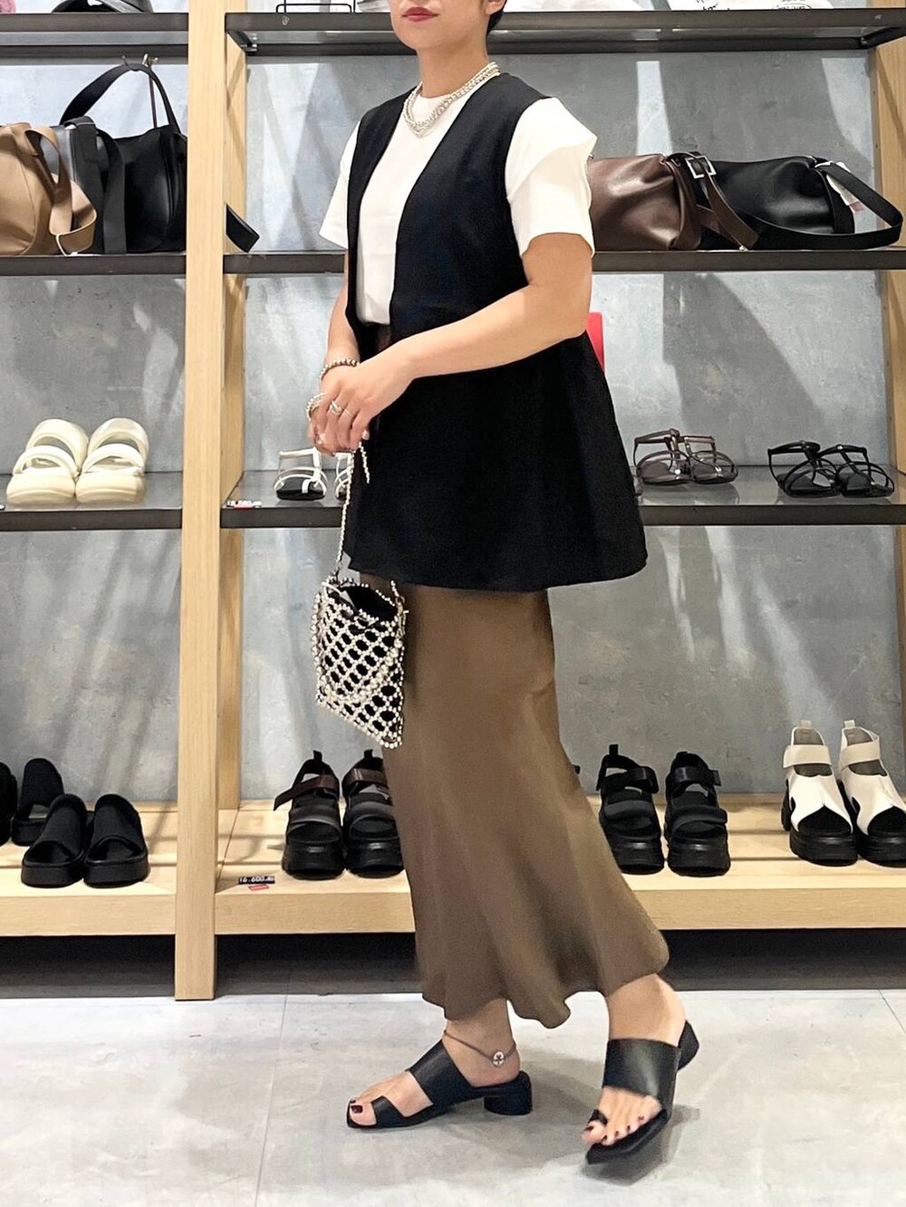 シルバー系のショルダーバッグ、ブラウン系のスカート、ブラック系のサンダルを着用したレディースの夏コーディネートの5枚目の写真