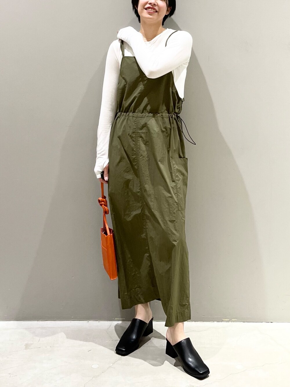 グリーン系のワンピース、オレンジ系のバッグ、ブラック系のサンダルを着用したレディースの春コーディネートの2枚目の写真