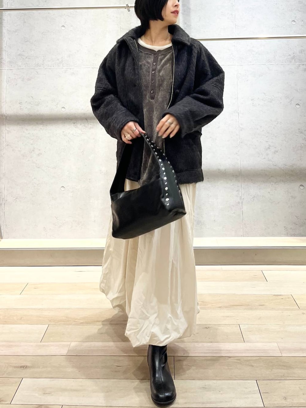 ブラック系のブーツ、ベージュ系のスカート、ブラック系のハンドバッグを着用したレディースの冬コーディネートの2枚目の写真