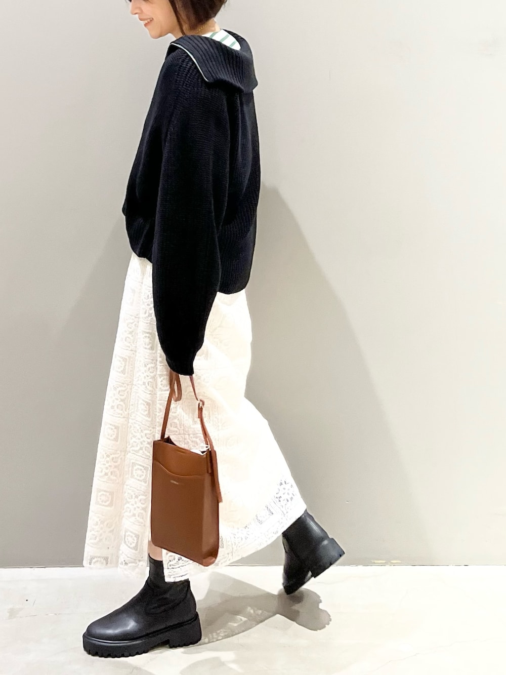 ブラウン系のショルダーバッグ、ホワイト系のスカート、ブラック系のブーツを着用したレディースの冬コーディネートの2枚目の写真