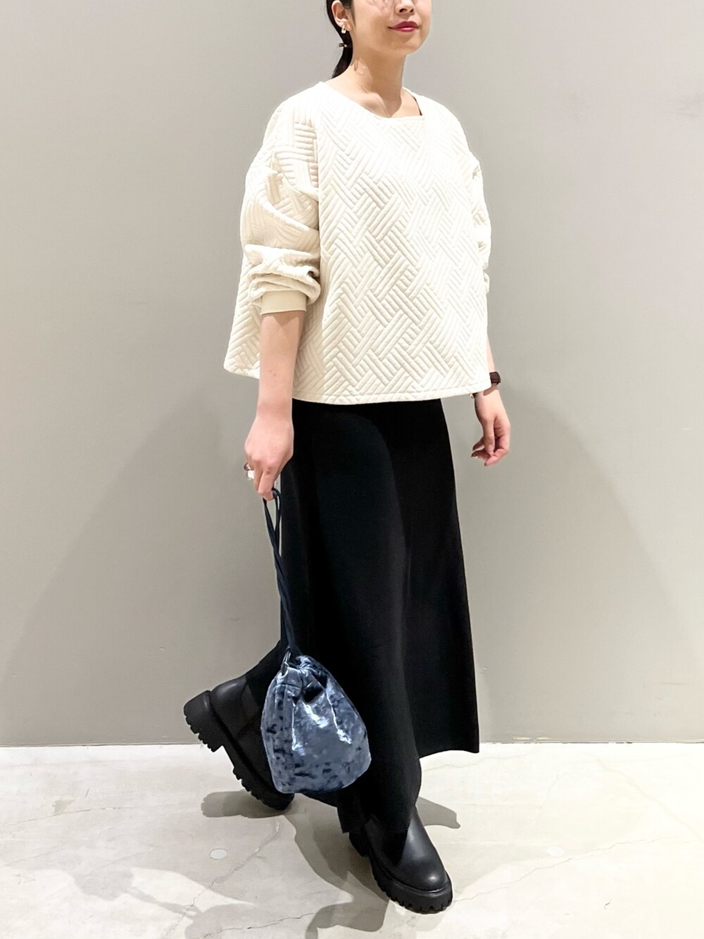 ブラック系のブーツ、ブラック系のスカート、ブルー系のショルダーバッグを着用したレディースの秋コーディネートの2枚目の写真