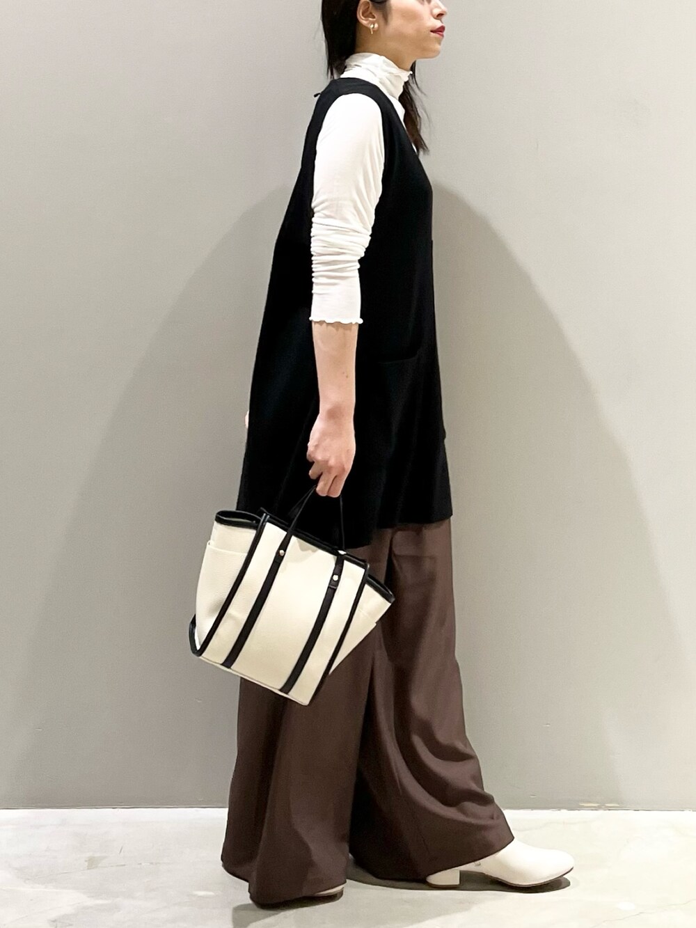 ホワイト系のショルダーバッグ、ブラック系のベスト、ブラック系のトップスを着用したレディースの秋コーディネートの2枚目の写真