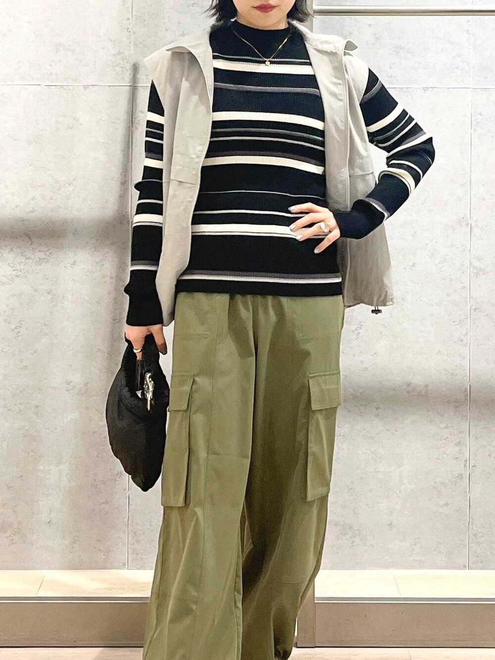 グレー系のベスト、ブラック系のハンドバッグ、グリーン系のカーゴパンツを着用したレディースの冬コーディネートの3枚目の写真