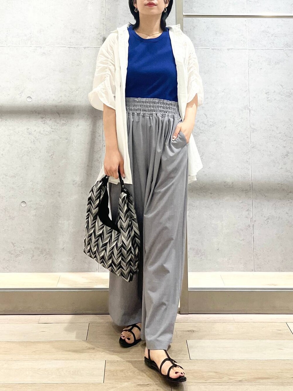 ブラック系のサンダル、ブラック系のハンドバッグ、グレー系のスラックスを着用したレディースの夏コーディネートの2枚目の写真