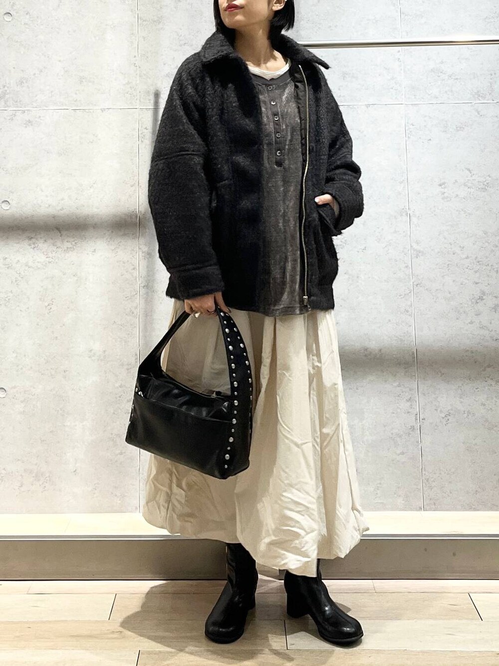 ブラック系のブーツ、ベージュ系のスカート、ブラック系のハンドバッグを着用したレディースの冬コーディネートの6枚目の写真