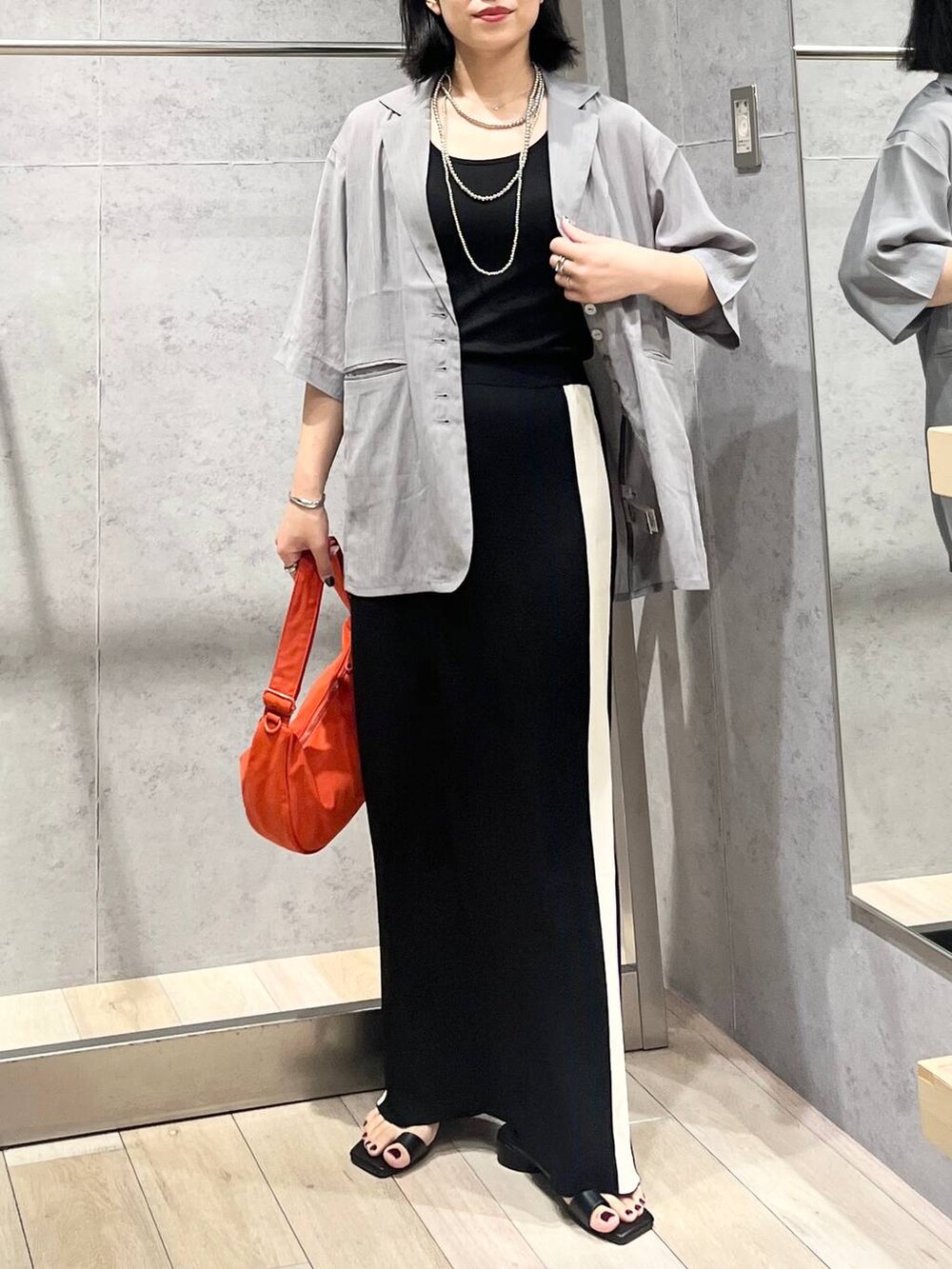 ブラック系のスカート、ブラック系のサンダル、オレンジ系のショルダーバッグを着用したレディースの夏コーディネートの2枚目の写真