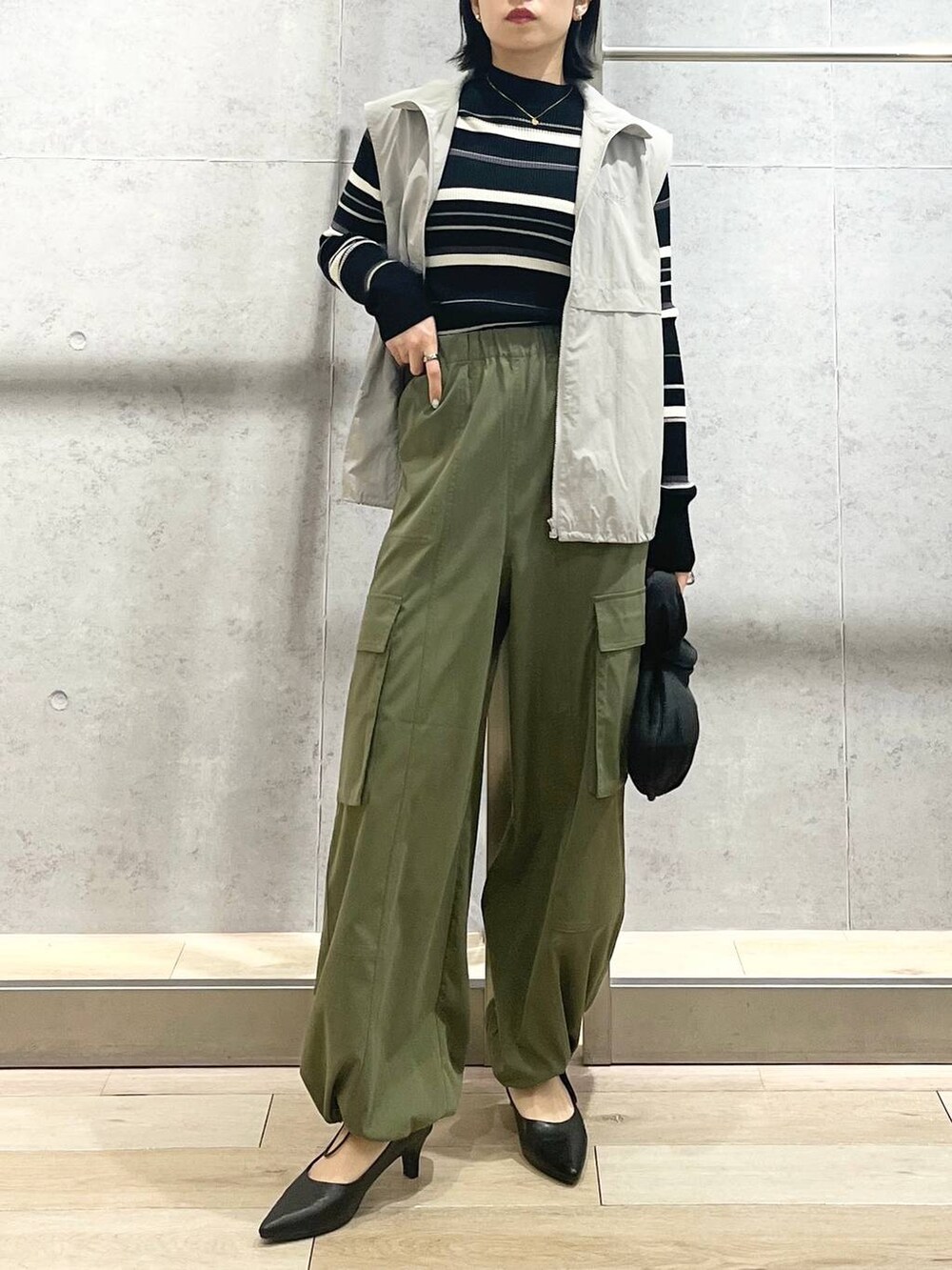 グレー系のベスト、ブラック系のハンドバッグ、グリーン系のカーゴパンツを着用したレディースの冬コーディネートの6枚目の写真