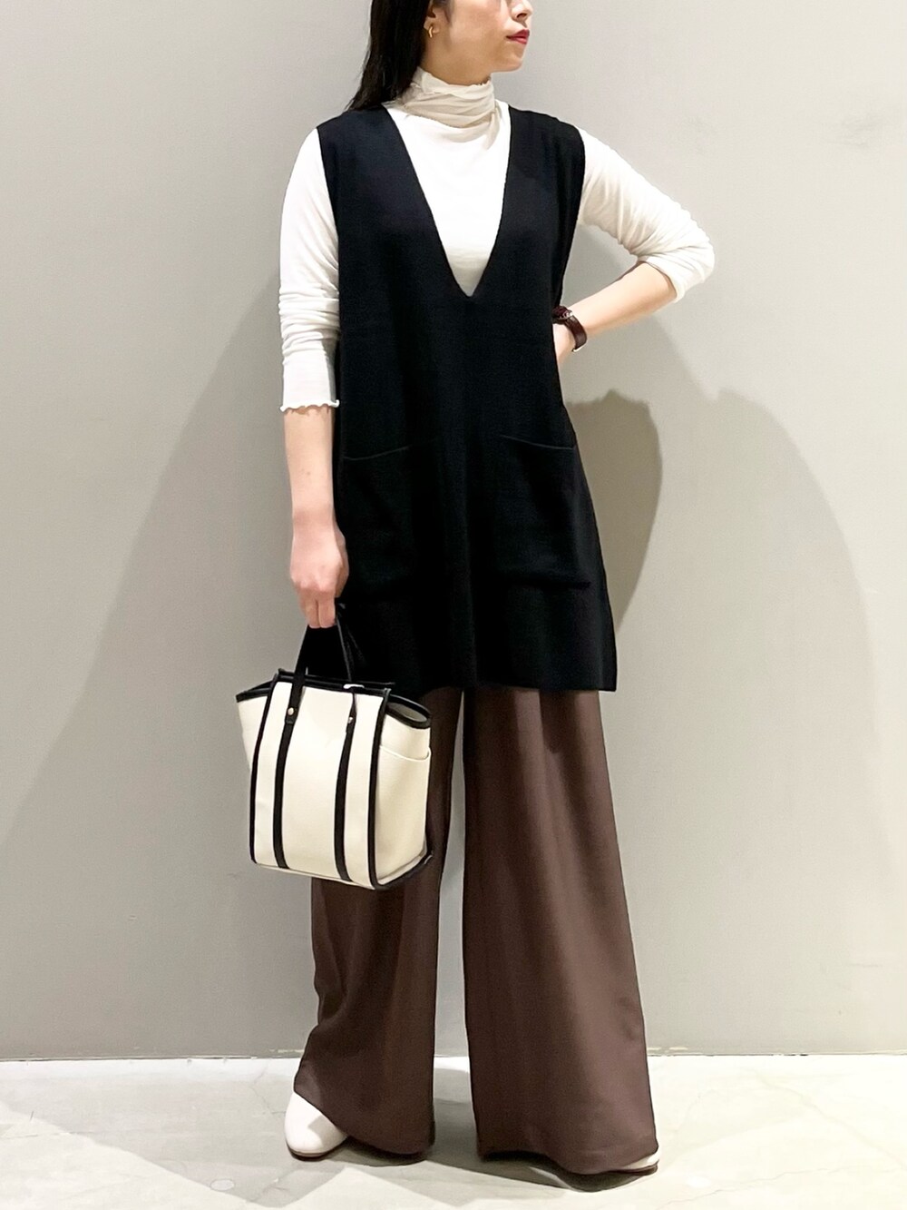 ホワイト系のショルダーバッグ、ブラック系のベスト、ブラック系のトップスを着用したレディースの秋コーディネートの4枚目の写真