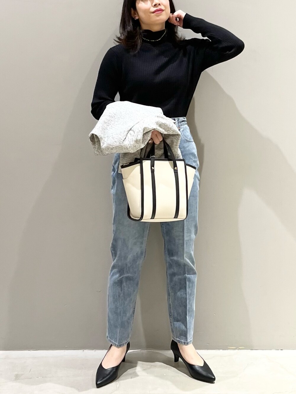 ブルー系のデニムパンツ、ブラック系のパンプス、ホワイト系のショルダーバッグを着用したレディースの冬コーディネートの3枚目の写真