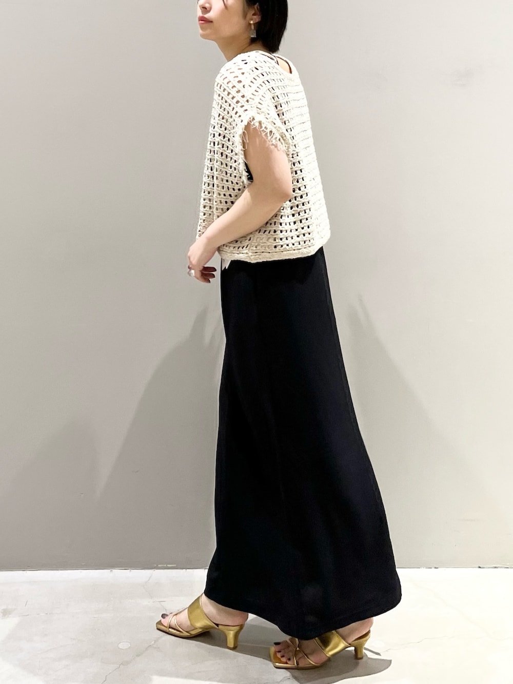 ホワイト系のショルダーバッグ、ブラック系のジャンパースカート、ゴールド系のサンダルを着用したレディースの夏コーディネートの2枚目の写真