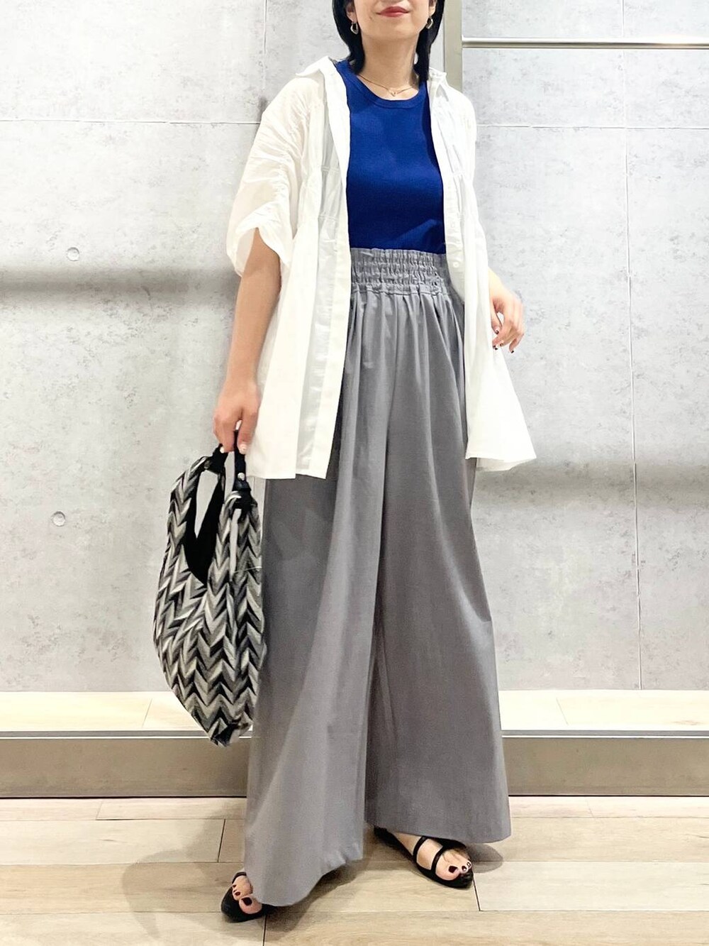 ブラック系のサンダル、ブラック系のハンドバッグ、グレー系のスラックスを着用したレディースの夏コーディネートの8枚目の写真