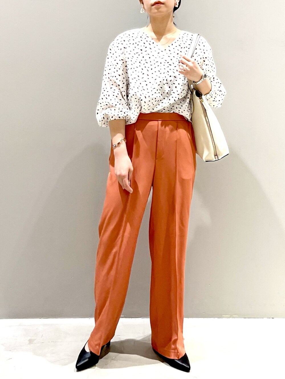 ホワイト系のシャツ/ブラウス、オレンジ系のスラックス、ブラック系のパンプスを着用したレディースの秋コーディネートの2枚目の写真