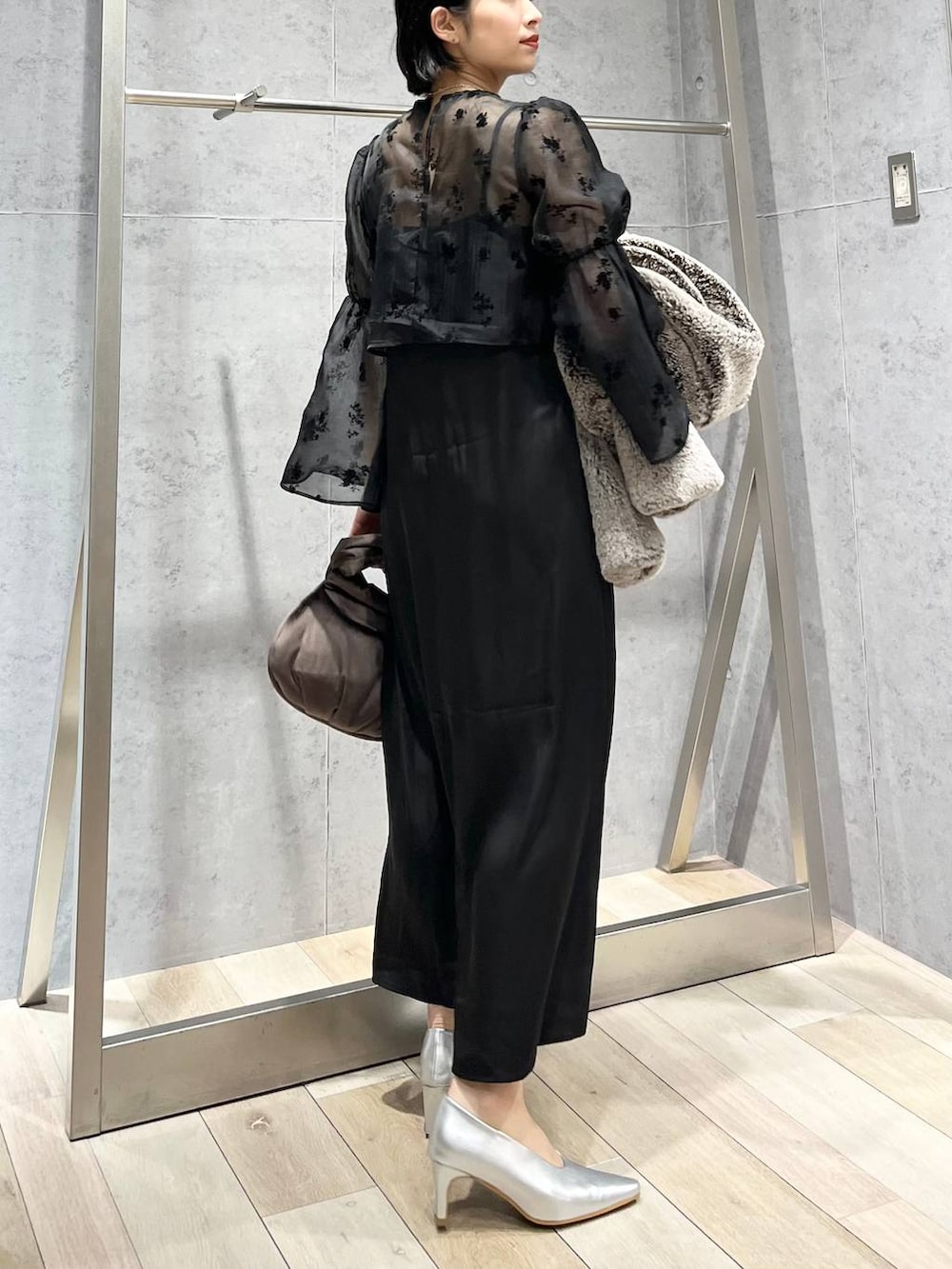 シルバー系のパンプス、ブラウン系のハンドバッグ、ベージュ系のノーカラーコートを着用したレディースの秋コーディネートの4枚目の写真