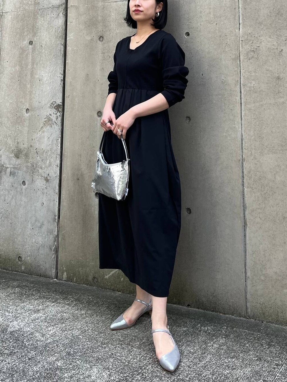 シルバー系のハンドバッグ、ブラック系のワンピース、グレー系のパンプスを着用したレディースの冬コーディネートの2枚目の写真