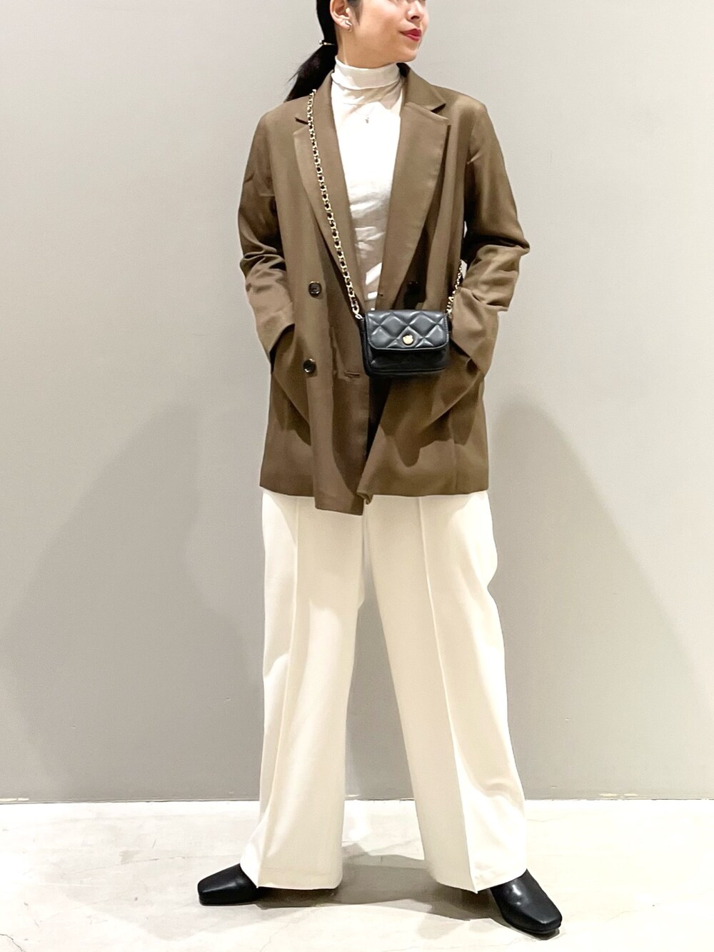 ホワイト系のスラックス、ブラック系のブーツ、ブラック系のバッグを着用したレディースの秋コーディネートの2枚目の写真
