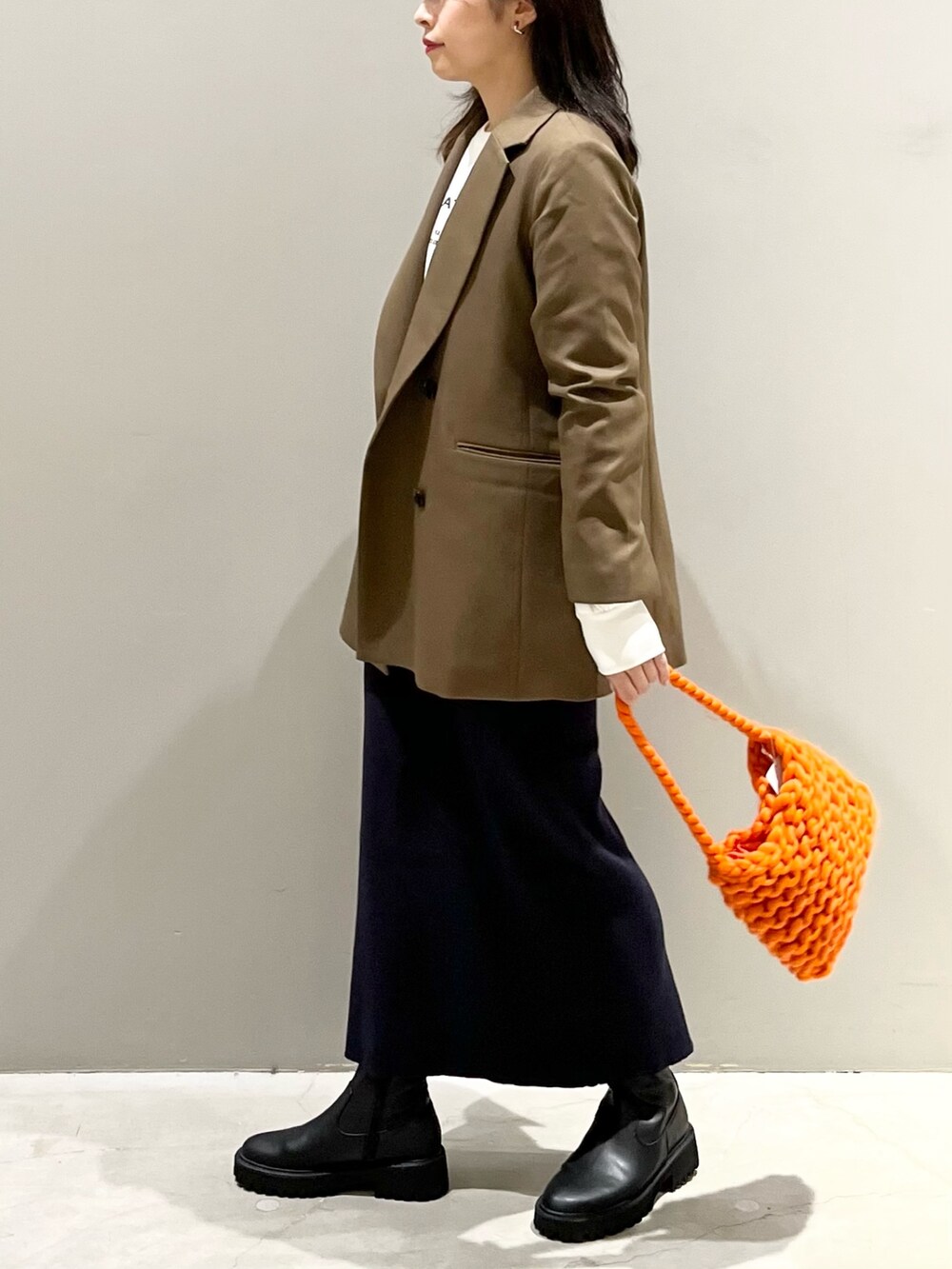 ブラック系のブーツ、ブルー系のスカート、オレンジ系のショルダーバッグを着用したレディースの秋コーディネートの2枚目の写真