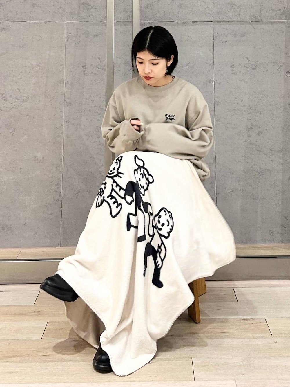 シルバー系のスカート、ブラック系のブーツ、ベージュ系のスウェットを着用したレディースの秋コーディネートの2枚目の写真