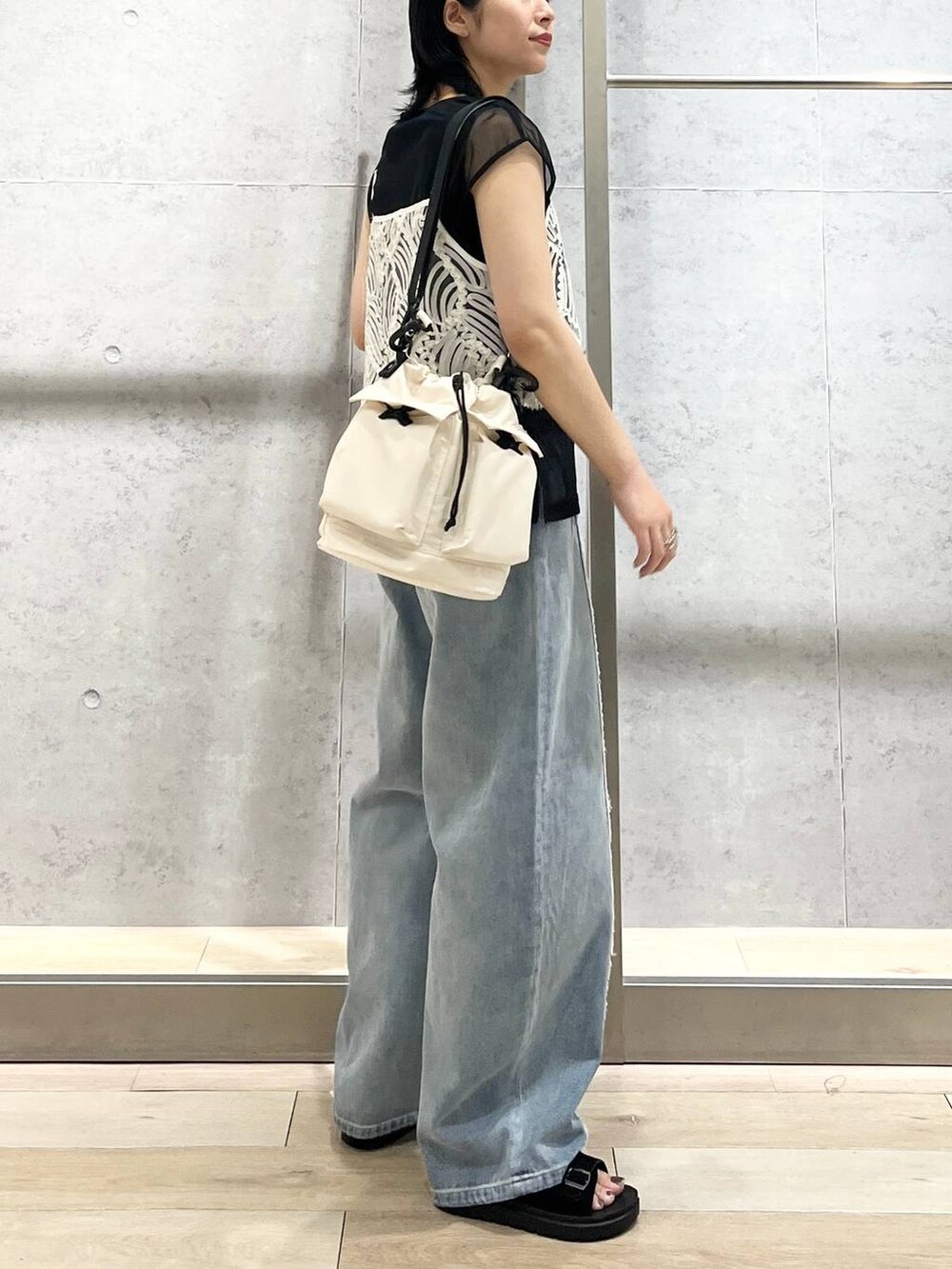 ホワイト系のショルダーバッグ、ブルー系のデニムパンツ、ブラック系のサンダルを着用したレディースの夏コーディネートの3枚目の写真