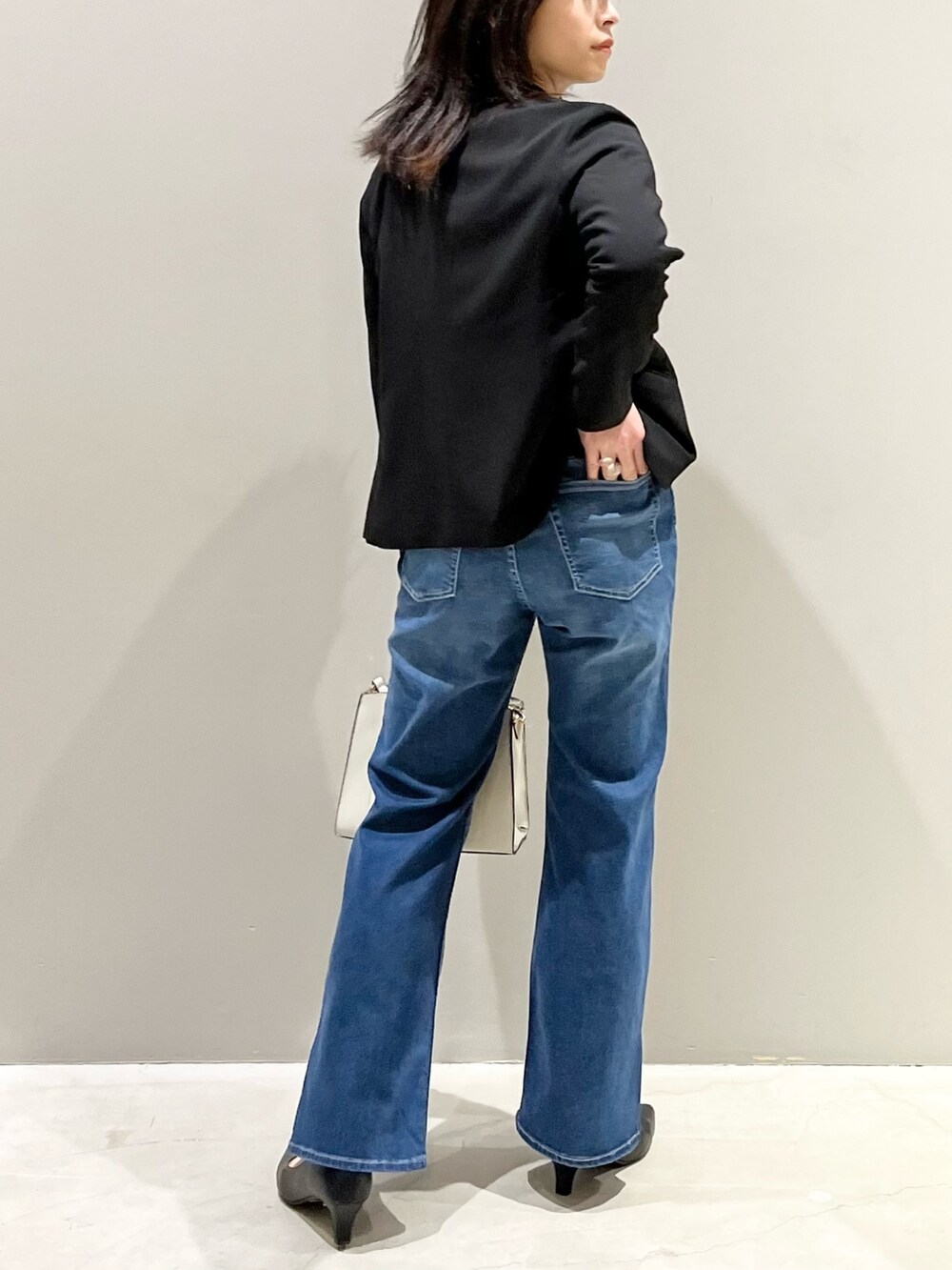 ブルー系のデニムパンツ、ブラック系のパンプス、ホワイト系のショルダーバッグを着用したレディースの秋コーディネートの2枚目の写真