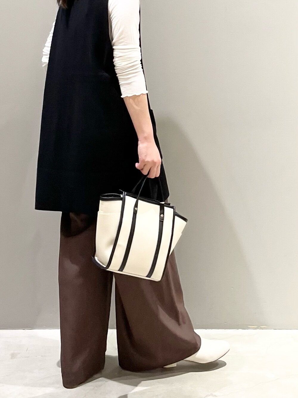 ホワイト系のショルダーバッグ、ブラック系のベスト、ブラック系のトップスを着用したレディースの秋コーディネートの3枚目の写真