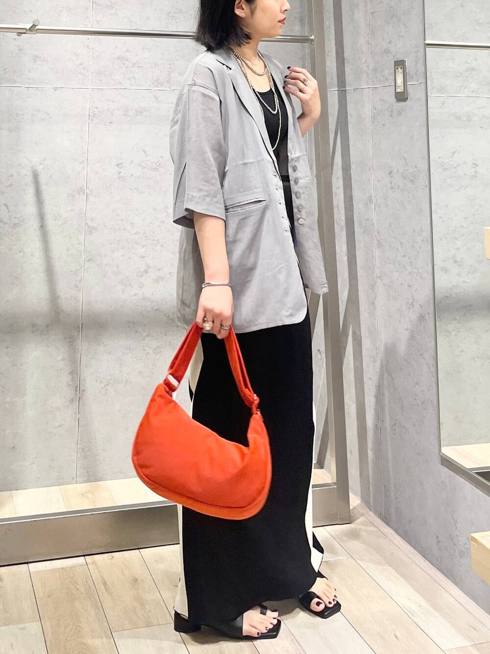 ブラック系のスカート、ブラック系のサンダル、オレンジ系のショルダーバッグを着用したレディースの夏コーディネートの3枚目の写真