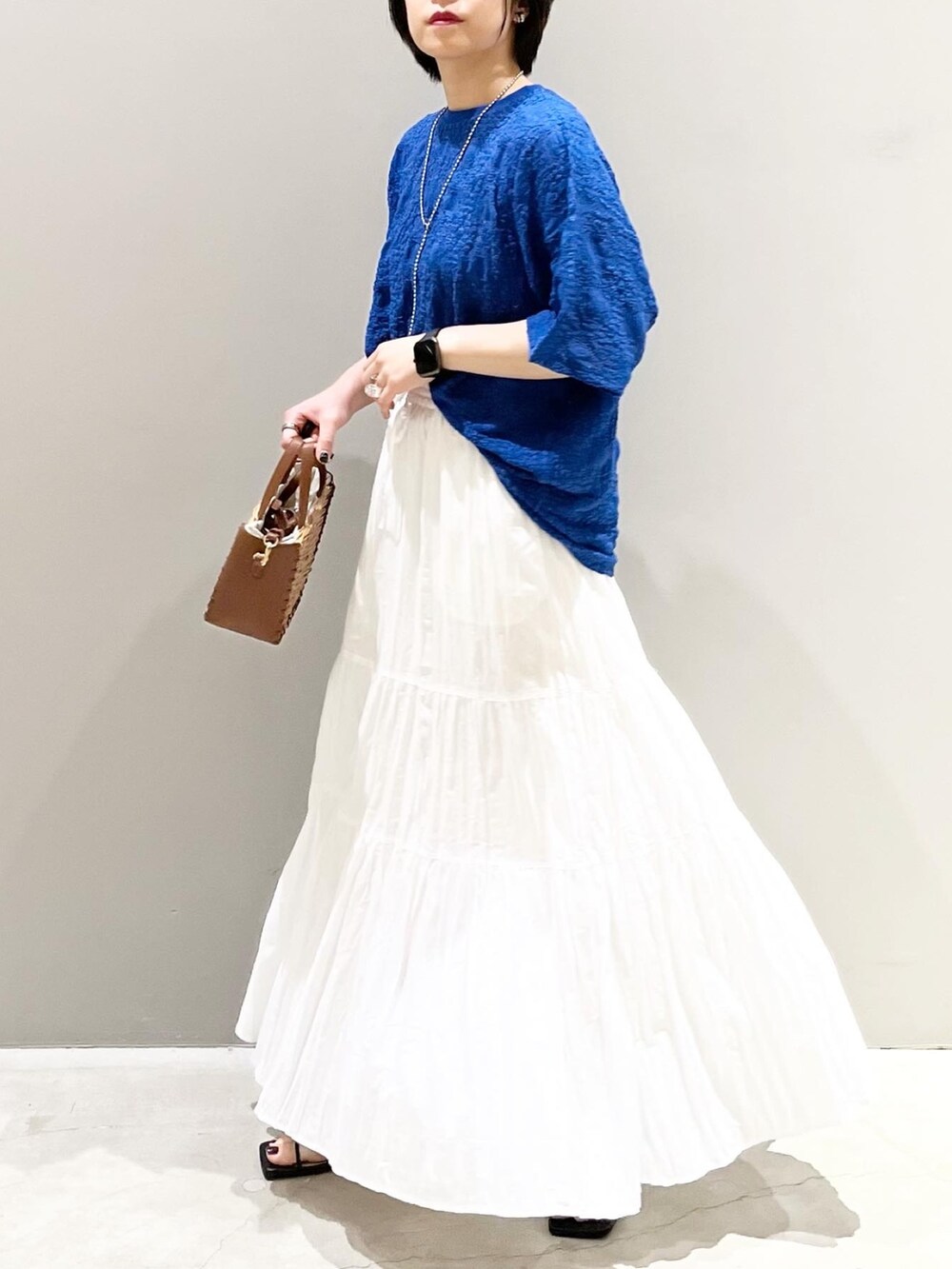 ブラック系のサンダル、ブラウン系のショルダーバッグ、ホワイト系のスカートを着用したレディースの夏コーディネートの5枚目の写真