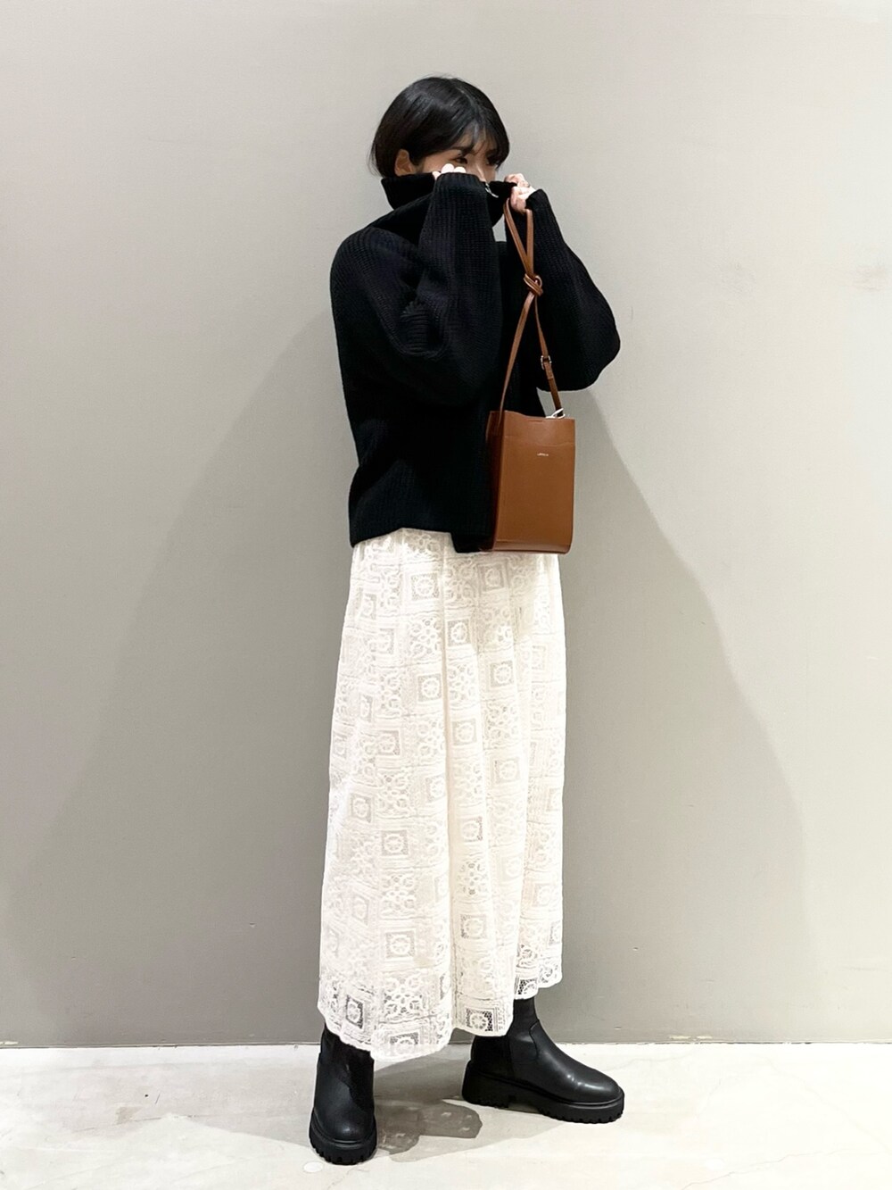 ブラウン系のショルダーバッグ、ホワイト系のスカート、ブラック系のブーツを着用したレディースの冬コーディネートの3枚目の写真