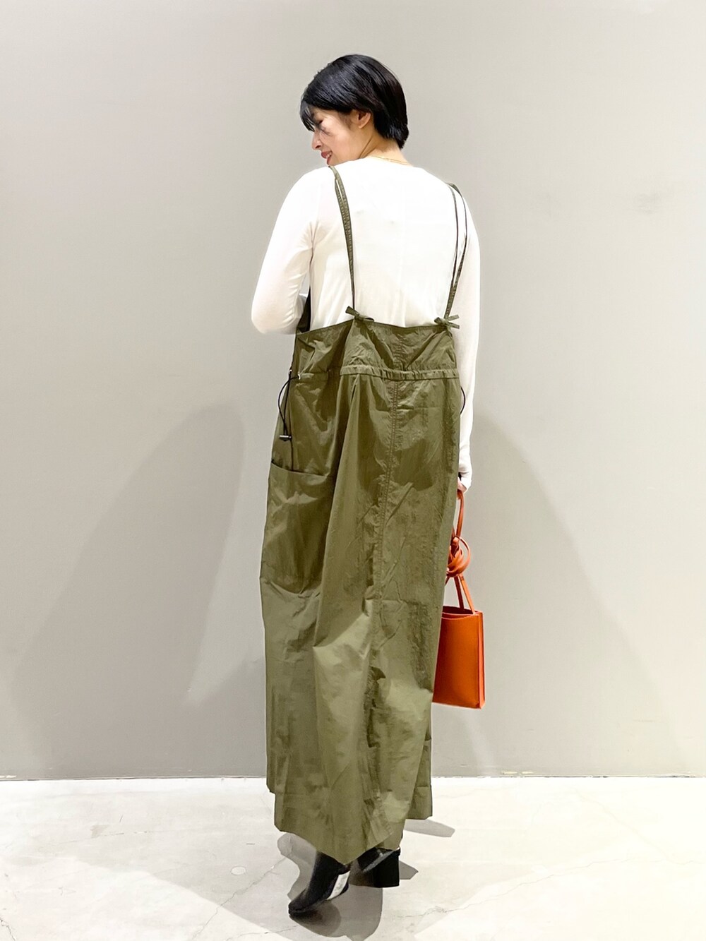 グリーン系のワンピース、オレンジ系のバッグ、ブラック系のサンダルを着用したレディースの春コーディネートの5枚目の写真