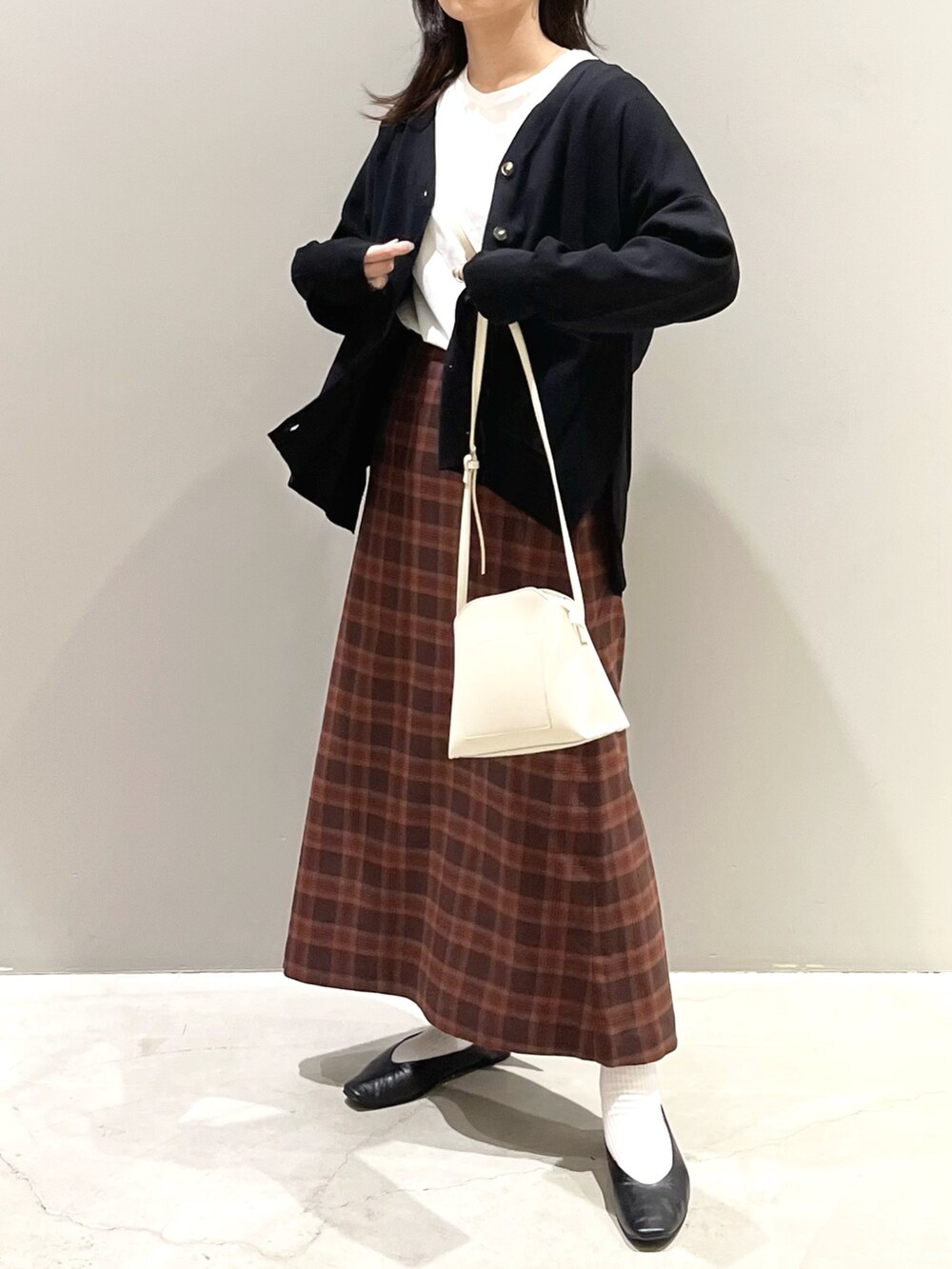 レッド系のスカート、ブラック系のパンプス、ホワイト系のショルダーバッグを着用したレディースの秋コーディネートの2枚目の写真