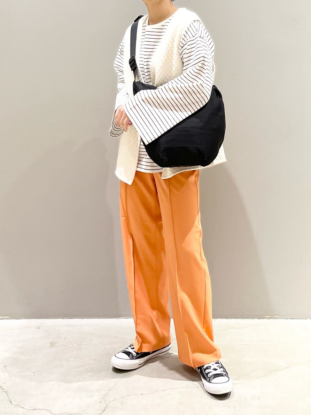 ブラック系のスニーカー、オレンジ系のスラックス、ホワイト系のトップスを着用したレディースの春コーディネートの5枚目の写真