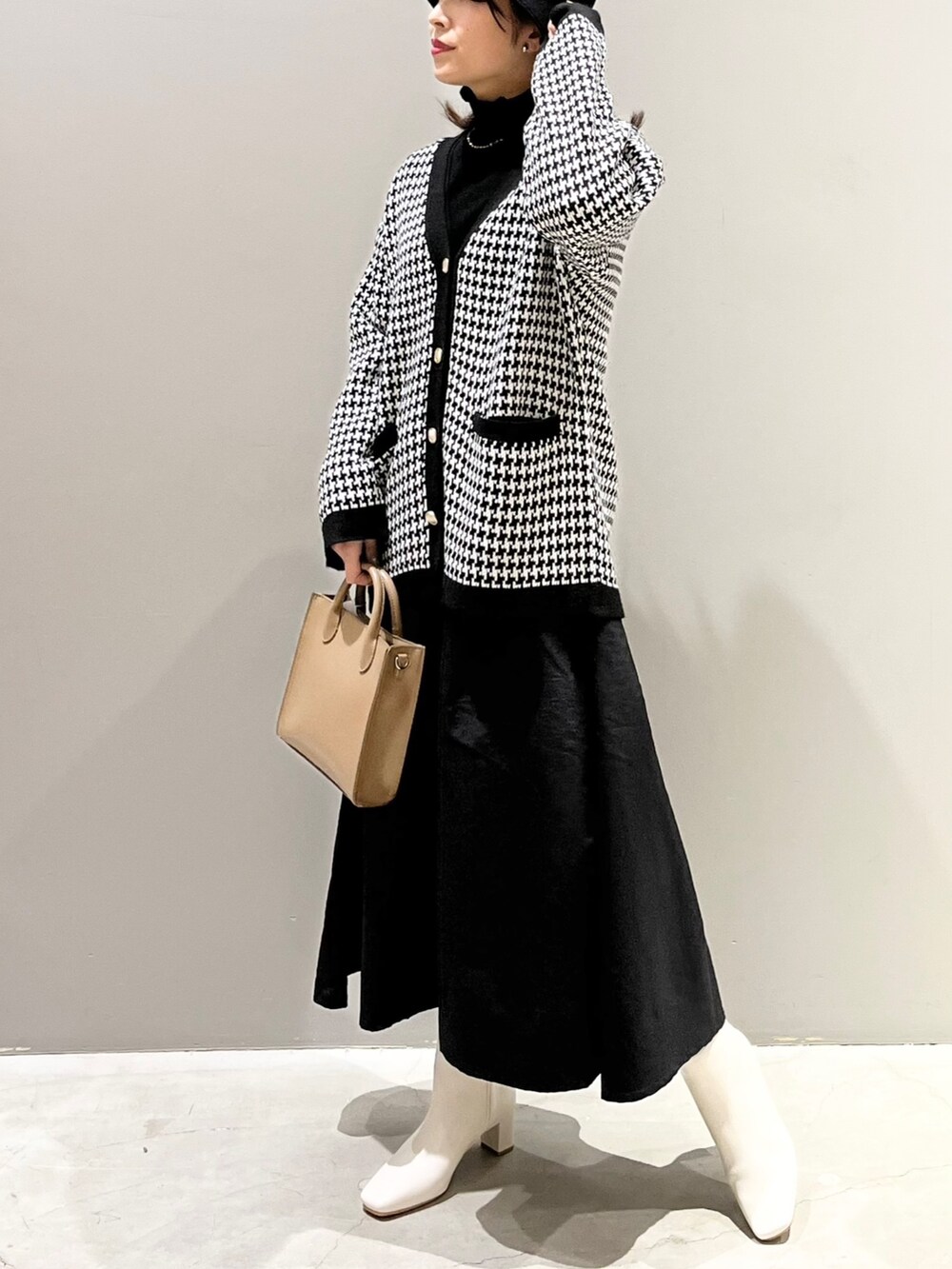 ベージュ系のショルダーバッグ、ホワイト系のブーツ、ブラック系のワンピースを着用したレディースの冬コーディネートの4枚目の写真