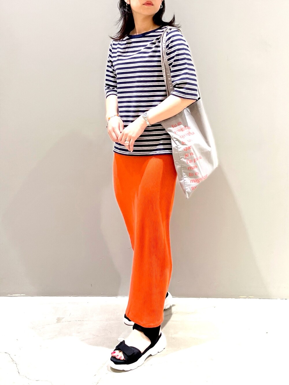 ブラック系のサンダル、オレンジ系のスカート、グレー系のトートバッグを着用したレディースの秋コーディネートの2枚目の写真