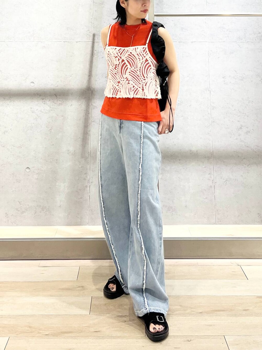 オレンジ系のタンクトップ、ブラック系のショルダーバッグ、ブルー系のデニムパンツを着用したレディースの夏コーディネートの7枚目の写真