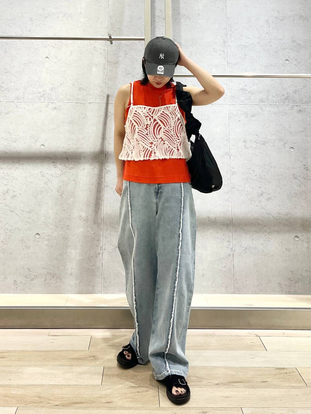 オレンジ系のタンクトップ、ブラック系のショルダーバッグ、ブルー系のデニムパンツを着用したレディースの夏コーディネートの5枚目の写真