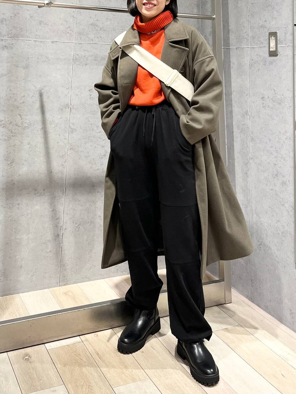 レッド系のニット/セーター、グリーン系のチェスターコート、ブラック系のブーツを着用したレディースの冬コーディネートの2枚目の写真