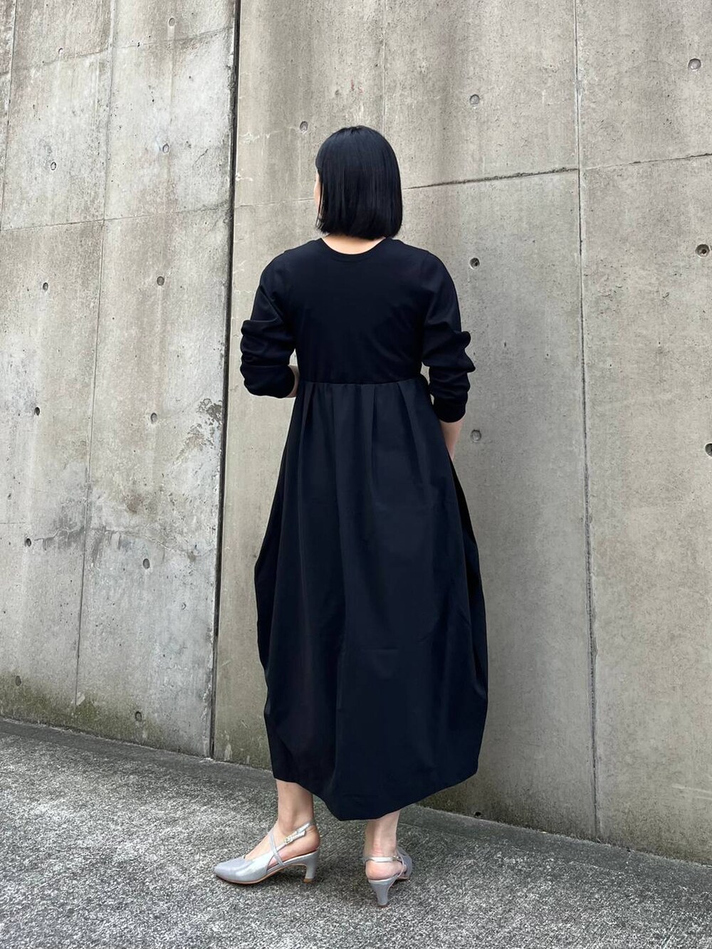 シルバー系のハンドバッグ、ブラック系のワンピース、グレー系のパンプスを着用したレディースの冬コーディネートの4枚目の写真