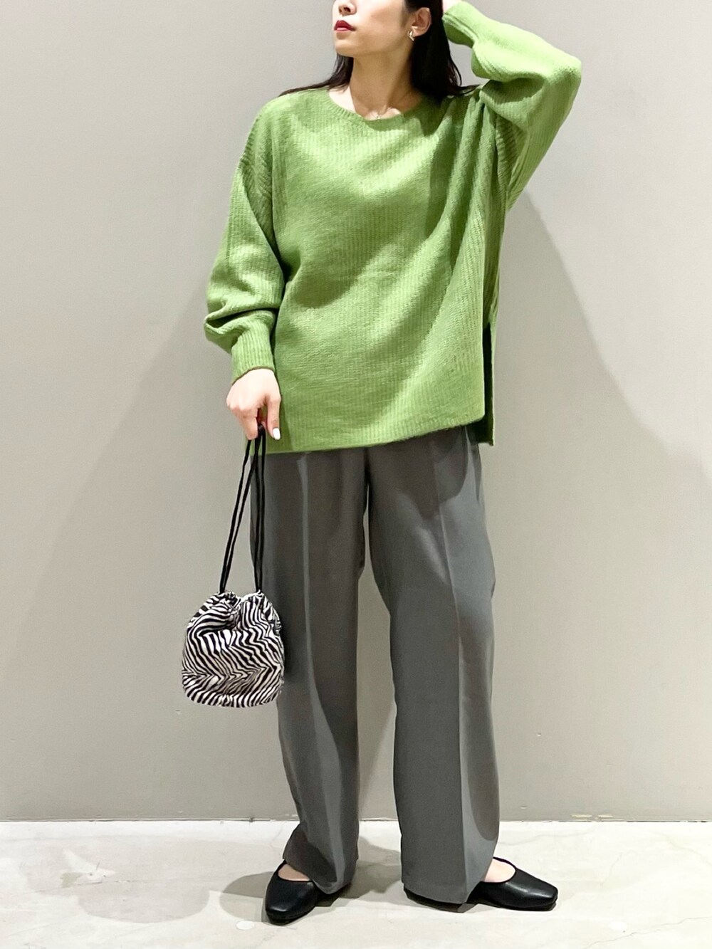 グリーン系のニット/セーター、ブラック系のパンプス、グレー系のパンツを着用したレディースの秋コーディネートの2枚目の写真