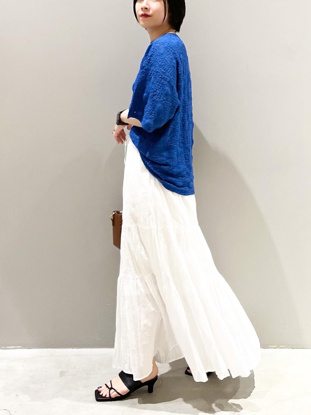 ブラック系のサンダル、ブラウン系のショルダーバッグ、ホワイト系のスカートを着用したレディースの夏コーディネートの3枚目の写真