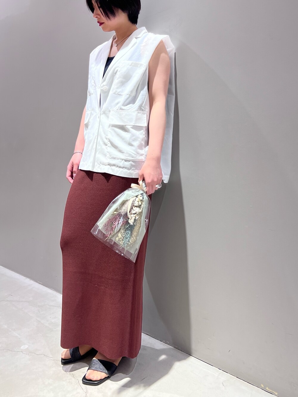 ホワイト系のベスト、ブラウン系のスカート、ブラック系のタンクトップを着用したレディースの春コーディネートの2枚目の写真