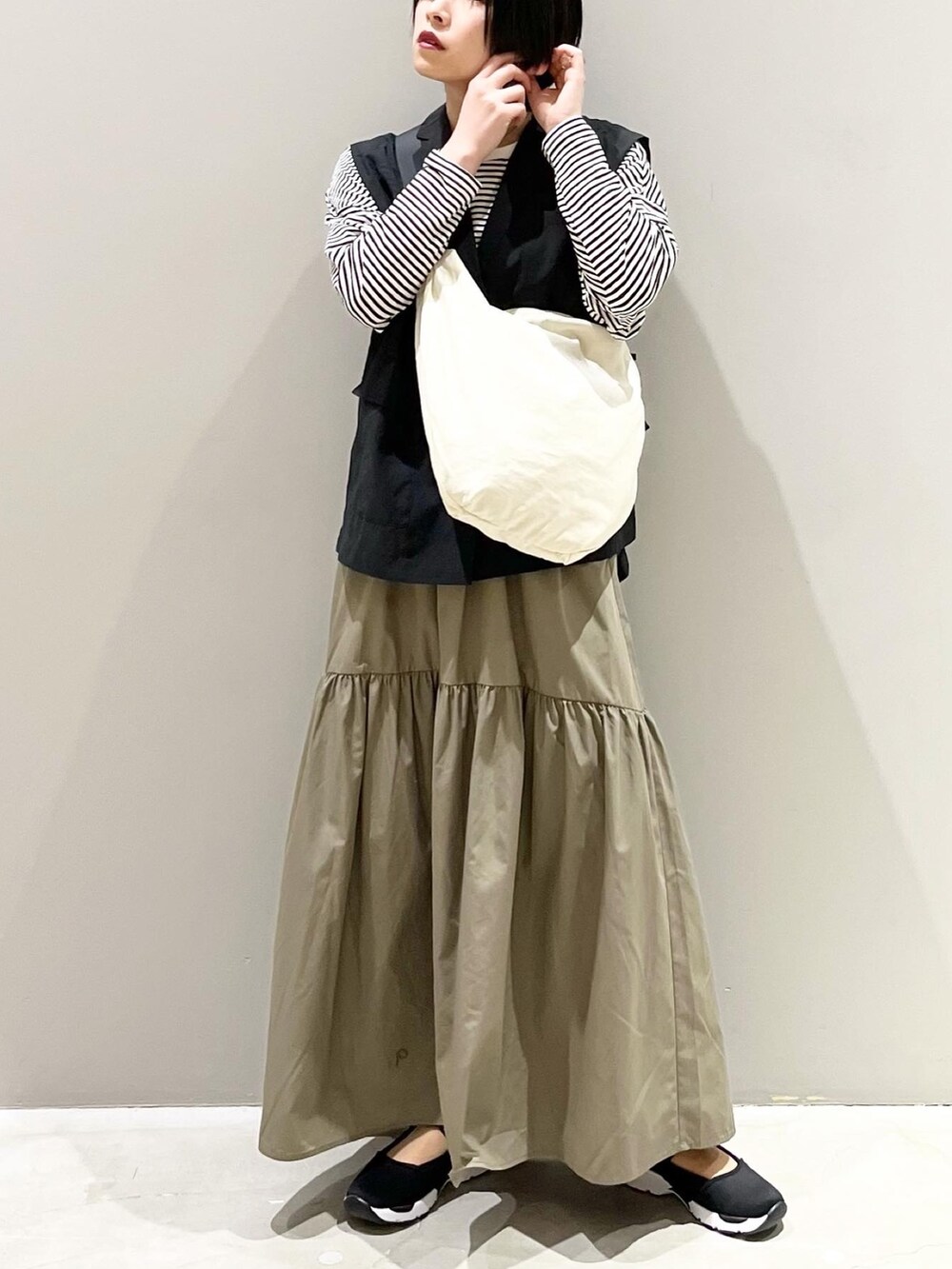 グリーン系のスカート、ブラック系のスニーカー、ホワイト系のショルダーバッグを着用したレディースの春コーディネートの2枚目の写真