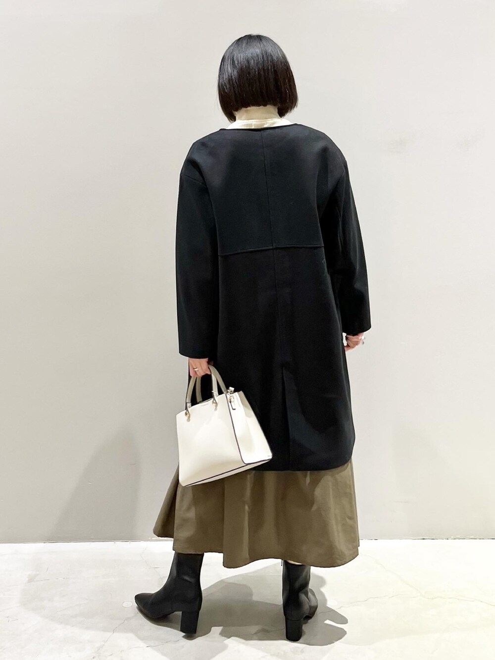 ブラック系のジャケット/アウター、グリーン系のワンピース、ホワイト系のショルダーバッグを着用したレディースの冬コーディネートの3枚目の写真