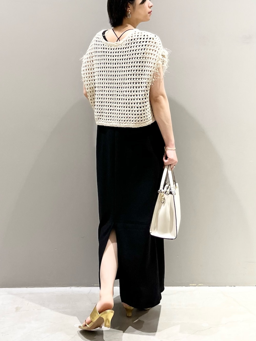ホワイト系のショルダーバッグ、ブラック系のジャンパースカート、ゴールド系のサンダルを着用したレディースの夏コーディネートの3枚目の写真