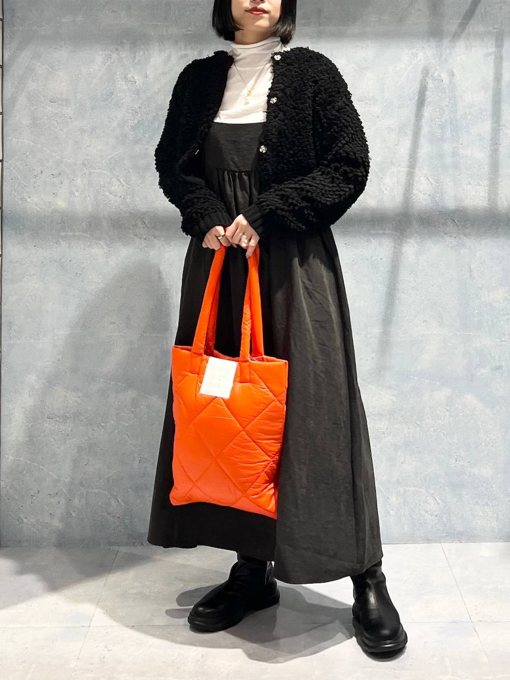 オレンジ系のトートバッグ、グレー系のワンピース、ブラック系のブーツを着用したレディースの冬コーディネートの5枚目の写真