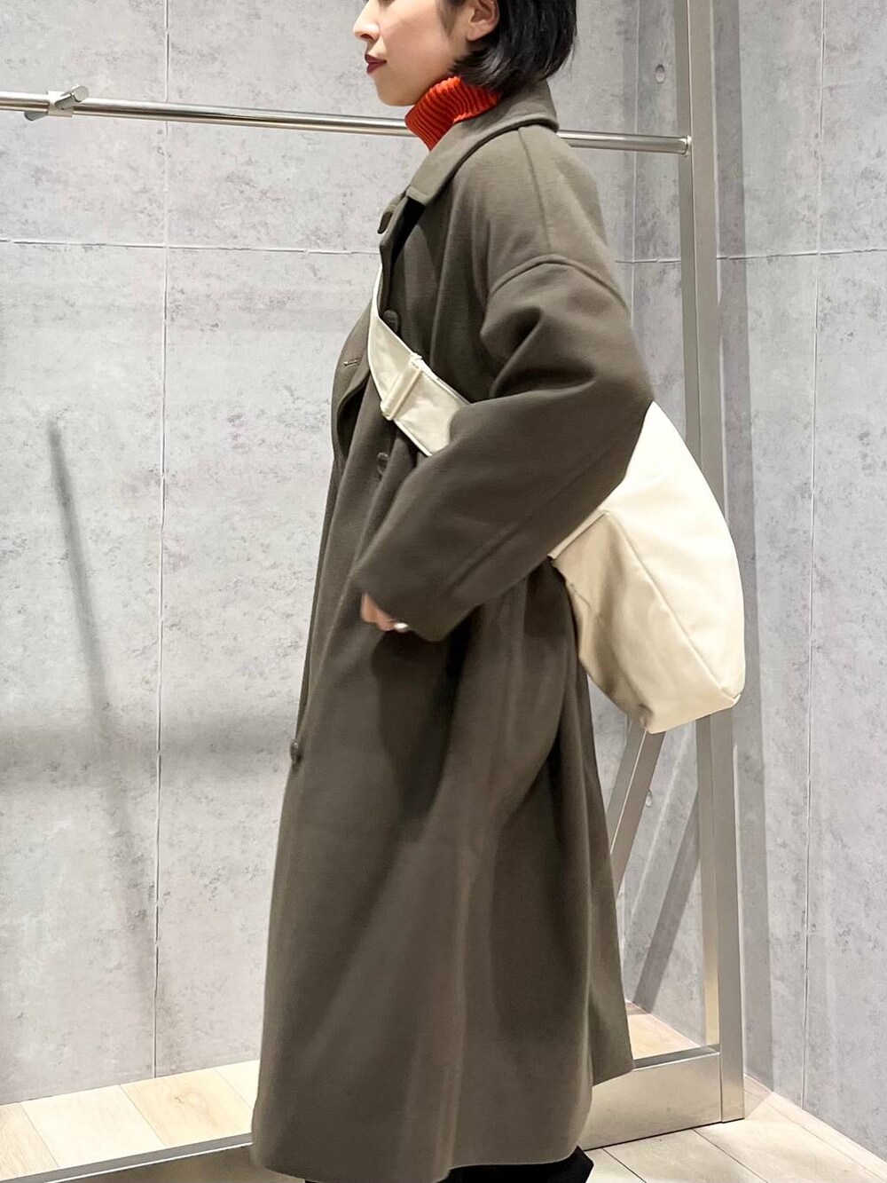 レッド系のニット/セーター、グリーン系のチェスターコート、ブラック系のブーツを着用したレディースの冬コーディネートの3枚目の写真