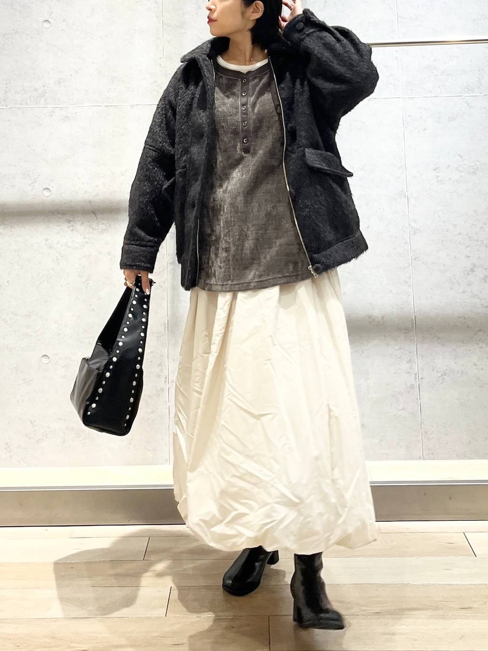 ブラック系のブーツ、ベージュ系のスカート、ブラック系のハンドバッグを着用したレディースの冬コーディネートの3枚目の写真