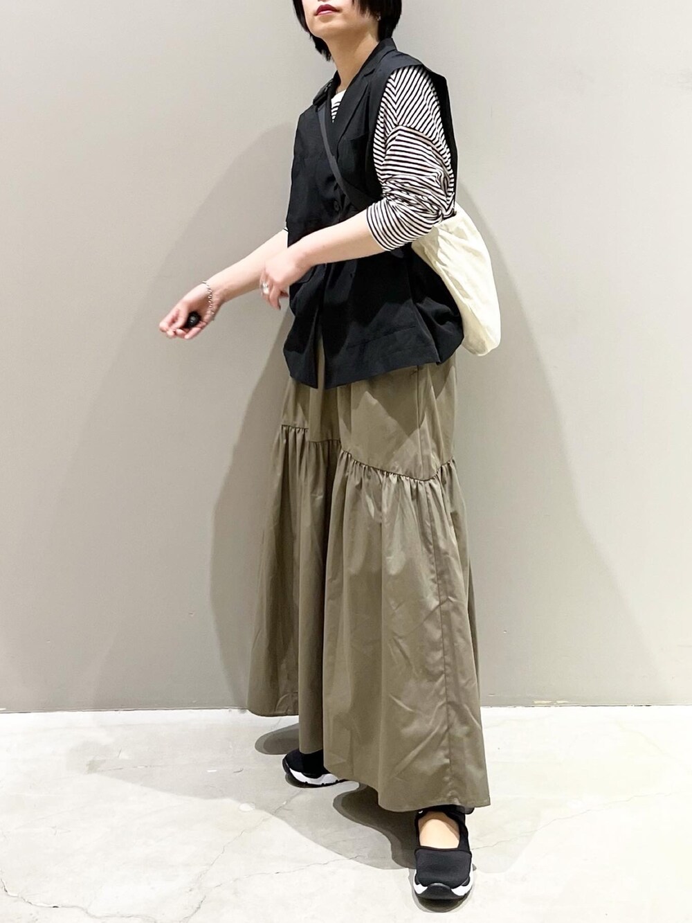 グリーン系のスカート、ブラック系のスニーカー、ホワイト系のショルダーバッグを着用したレディースの春コーディネートの3枚目の写真