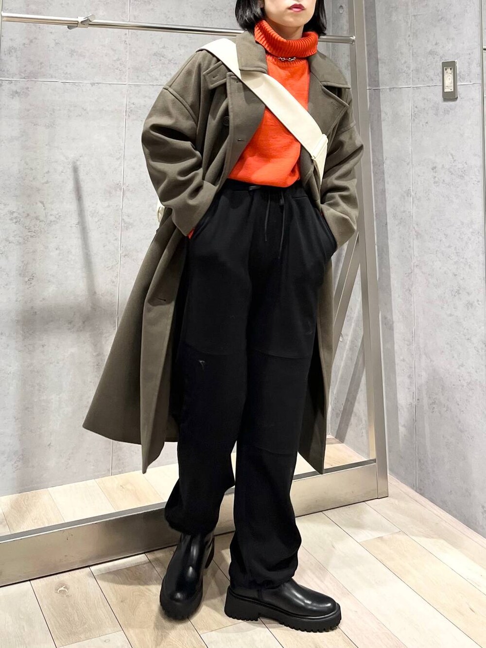 レッド系のニット/セーター、グリーン系のチェスターコート、ブラック系のブーツを着用したレディースの冬コーディネートの7枚目の写真